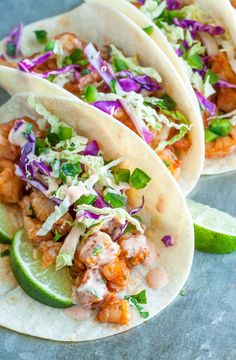 three fish tacos with cole slaw and lime wedges on a blue surface