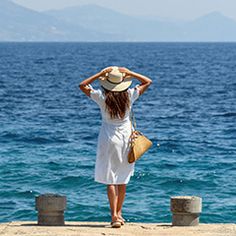 a woman in a white dress and straw hat looking out at the ocean