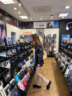 a woman walking through a store filled with lots of shelves full of books and cds