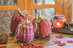 three pumpkins sitting on top of a wooden table next to a candle and some leaves