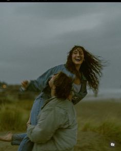 two people are playing in the sand on a cloudy day with their arms around each other