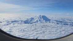 the view from an airplane window shows clouds and a snow capped mountain in the distance