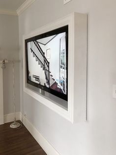 a flat screen tv mounted to the side of a white wall next to a wooden floor