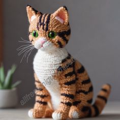 a crocheted cat sitting on top of a table next to a potted plant