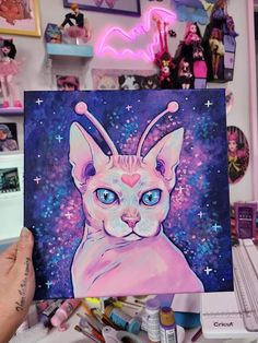 a person holding up a painting of a cat with blue eyes and stars in the background