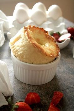 a pastry in a white dish with strawberries on the side and an egg shell behind it