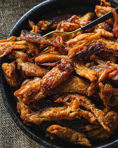 a bowl filled with cooked meat on top of a cloth covered table next to a fork