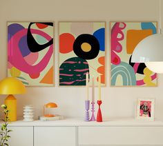 three abstract paintings hang on the wall above a white dresser and sideboard in a living room