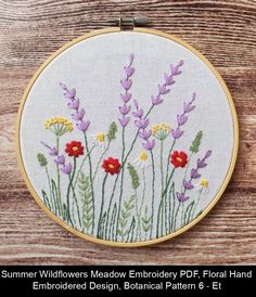 a cross stitch pattern with wildflowers and daisies in the grass on a wooden background