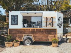 a small food truck parked on the side of a road with potted plants in front of it