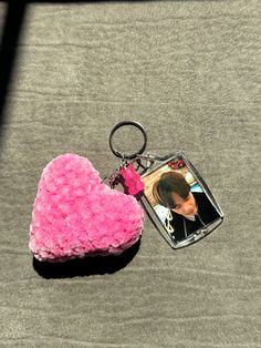 a pink heart shaped keychain sitting on top of a gray surface next to a photo