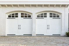 two white garage doors are open in front of a brick wall and stone flooring