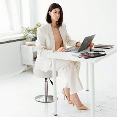 a woman sitting at a white desk with a laptop computer on her lap and papers in front of her