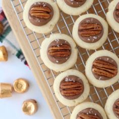 cookies with chocolate frosting and pecans on a cooling rack next to gold candies