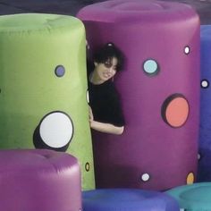 a woman is peeking out from behind several large inflatables that are all different colors