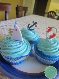 two cupcakes with blue frosting and a sailboat on top are sitting on a plate