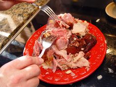 a red plate topped with meat and vegetables on top of a counter next to a knife and fork