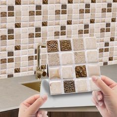 two hands are holding a white plate in front of a mosaic tile backsplash