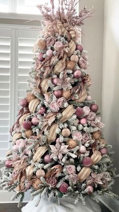 a decorated christmas tree with pink and gold ornaments on it's top, sitting in front of a window