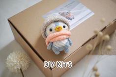 a small stuffed penguin with a knitted hat and scarf sits in front of a cardboard box