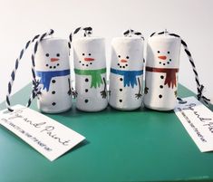 four snowmen wrapped in toilet paper on top of a green table with two tags attached to them