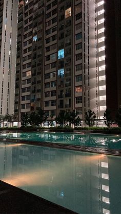 an empty swimming pool in the middle of a city at night with tall buildings behind it