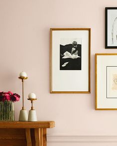 three framed pictures hang on the wall next to a table with vases and flowers