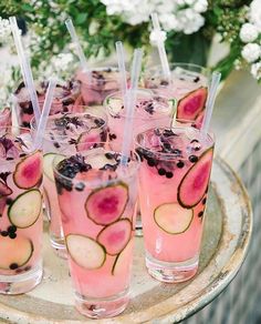 several glasses filled with drinks sitting on top of a wooden tray next to flowers and greenery