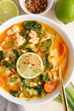 a white bowl filled with chicken and vegetable soup next to limes, cilantro, and other ingredients