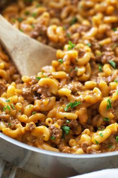 a skillet filled with macaroni and cheese being stirred by a wooden spoon