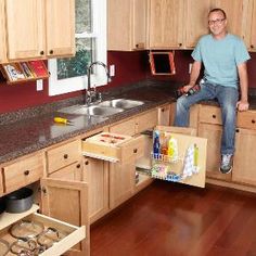 a man sitting on top of a kitchen counter next to an open cabinet drawer in front of him