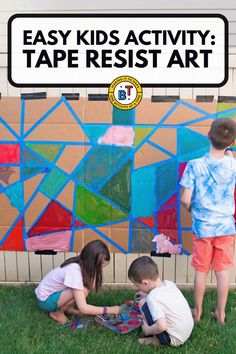 three children are playing with tape resist art on the grass in front of a cardboard box