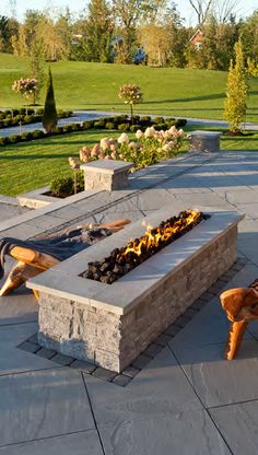 a fire pit sitting on top of a stone patio next to a lush green field