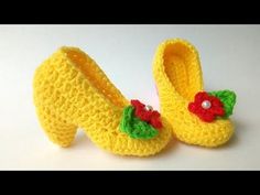 crocheted yellow slippers with red flowers and green leaves on the bottom, sitting on a white surface