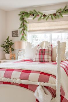 a bedroom decorated for christmas with red and white bedding, plaid pillows and garland