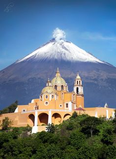 a large building sitting on top of a lush green hillside next to a snow covered mountain