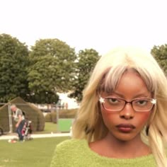 a woman with blonde hair and glasses standing in front of a fenced park area