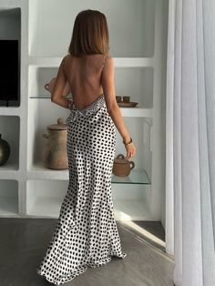 the back of a woman in a polka dot print dress looking at shelves with vases