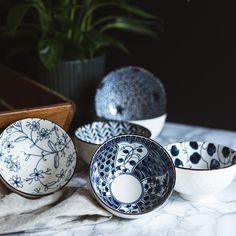 four bowls with designs on them sitting on a marble counter top next to a potted plant