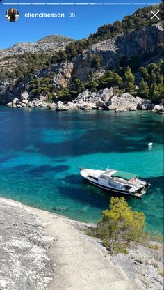 a boat floating on top of a body of water next to a rocky hillside covered with trees