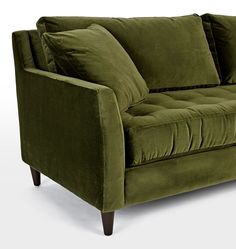 a green velvet couch with two pillows on it's arms and backrests