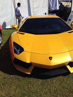 a yellow sports car parked on top of a lush green field next to a white tent