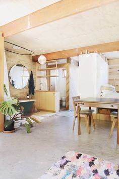 a room with a table, chairs and a refrigerator in the corner next to a potted plant