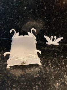 two white swans sitting on top of a black marble counter next to another swan shaped object