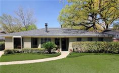 a house that is in the middle of some grass and trees with bushes around it