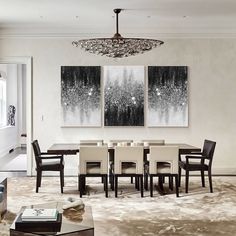 a dining room table and chairs in front of two paintings on the wall above it