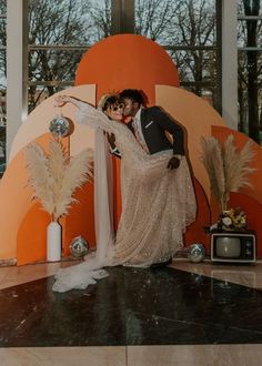 a man and woman posing for a photo in front of an orange wall with feathers