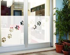 an open sliding glass door with dog paw prints on the side and potted plants in front