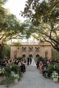 a wedding ceremony in front of an old building with lots of greenery and white flowers