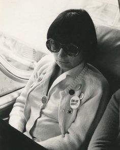 a woman sitting on an airplane seat wearing sunglasses and looking at her cell phone in front of the window